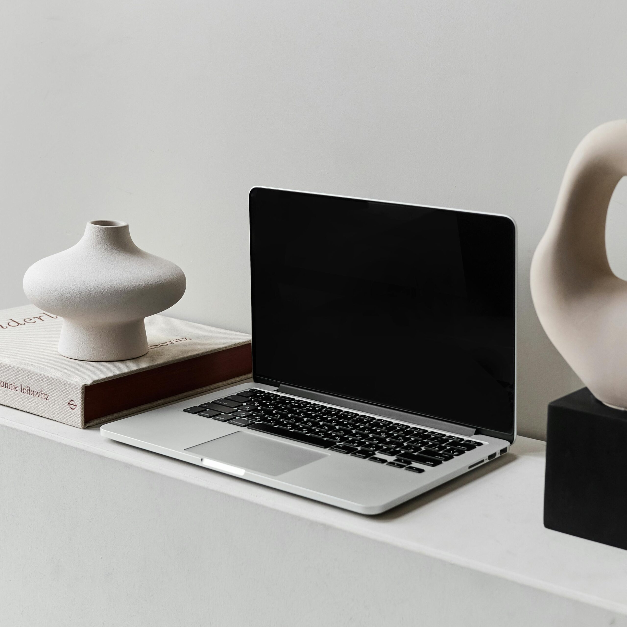 A sleek laptop on a modern desk alongside stylish ceramic vases, embodying minimalism.