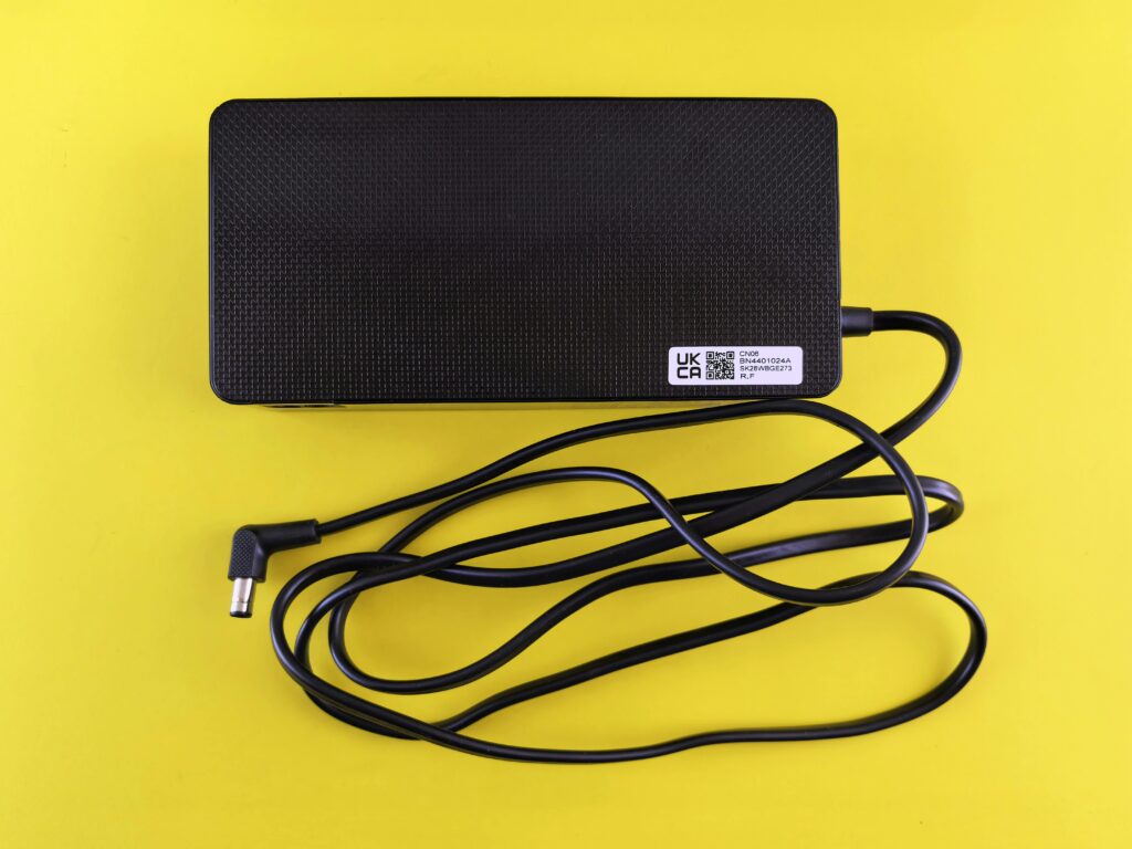 A black power adapter with cord on a vibrant yellow background, showcasing electronics.