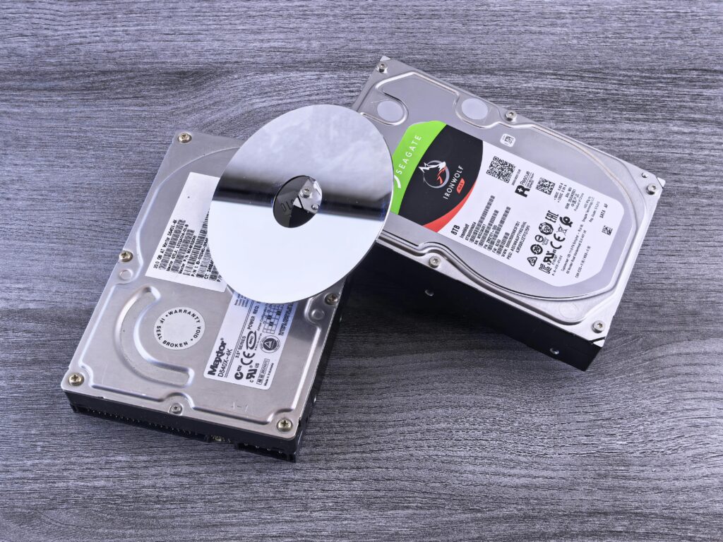 Two computer hard drives and a shiny disk displayed on a wooden surface.