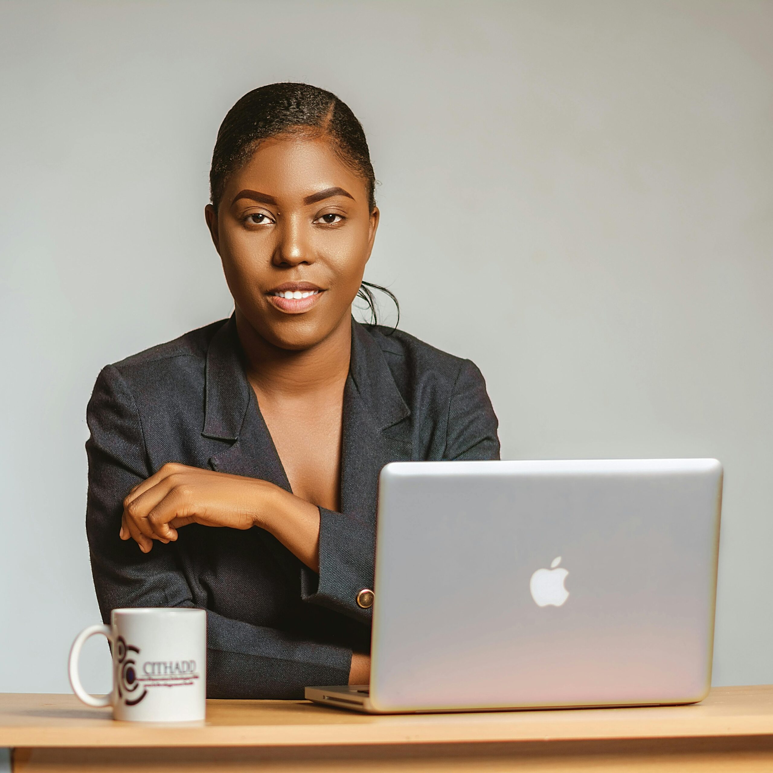 Confident black woman in blazer using laptop at wooden desk.