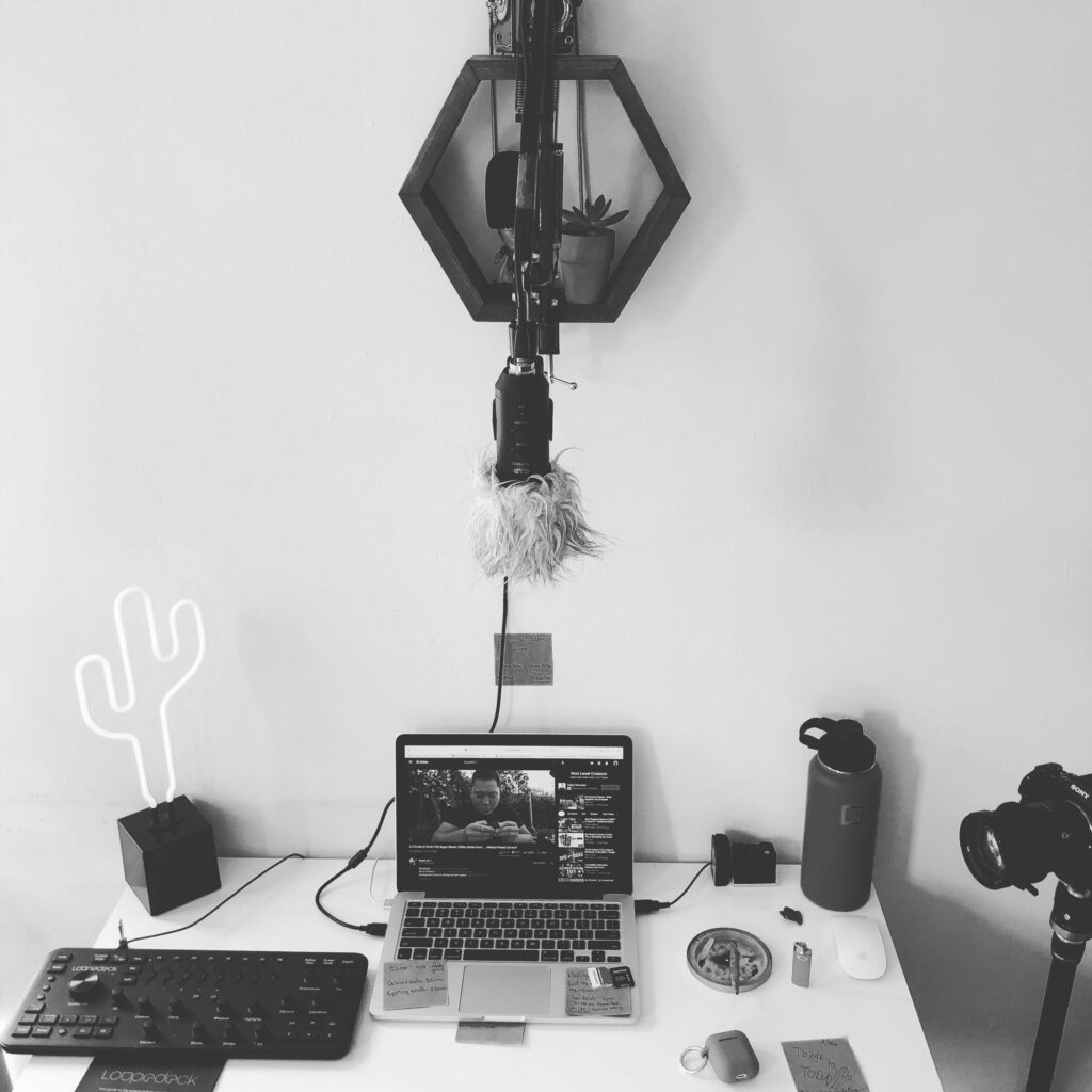 A minimalist black and white home recording studio setup with a laptop, microphone, camera, and creative equipment.
